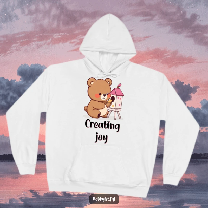 Funny cute bear painting a colorful birdhouse with a tiny brush, on a cozy hoodie, a humorous and artistic gift.