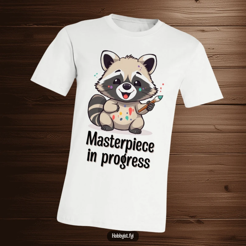 Funny raccoon wearing paint splatters on its face, holding a brush, looking delighted, T-shirt design for art lovers and humor enthusiasts.